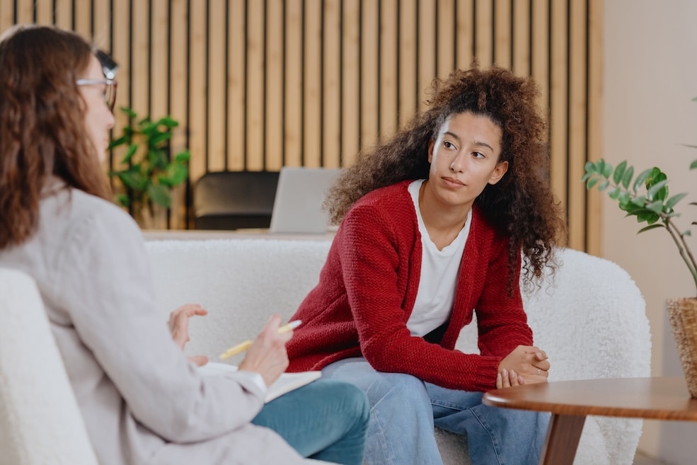 teenage girl and mom are sitting on a couch talking about mental health issues