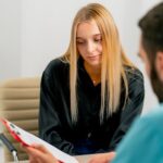 Teen girl with long blonde hair looking at medical results on clipboard her doctor is holding out and explaining to her