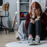 Teenage girl sitting on the floor and crying because of problems at home with parents, exhibiting signs of bipolar disorder in teens and in need of treatment