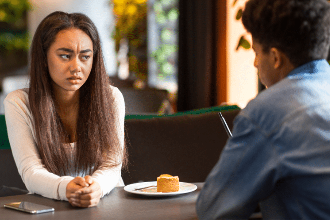 Teenage girl sitting at table looking angry at guy