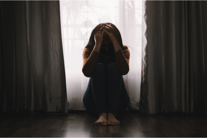 Angry teen girl sitting on floor beside curtains