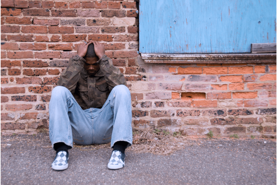 Boy sitting on the floor leaning against a wall with his head in his hands