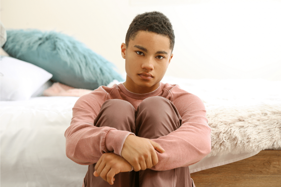 Angry teenager sitting on the floor leaning on his bed