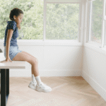 Girl student in room alone sitting on top of table looking down at the floor