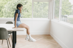 Girl student in room alone sitting on top of table looking down at the floor