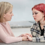 Mom sitting at table with daughter trying to comfort her and hold her hands
