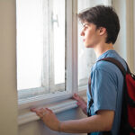Teen boy student looking out window with backpack on