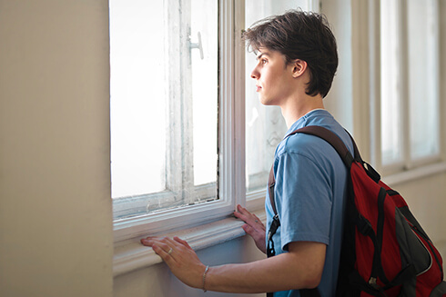 Teen boy student looking out window with backpack on
