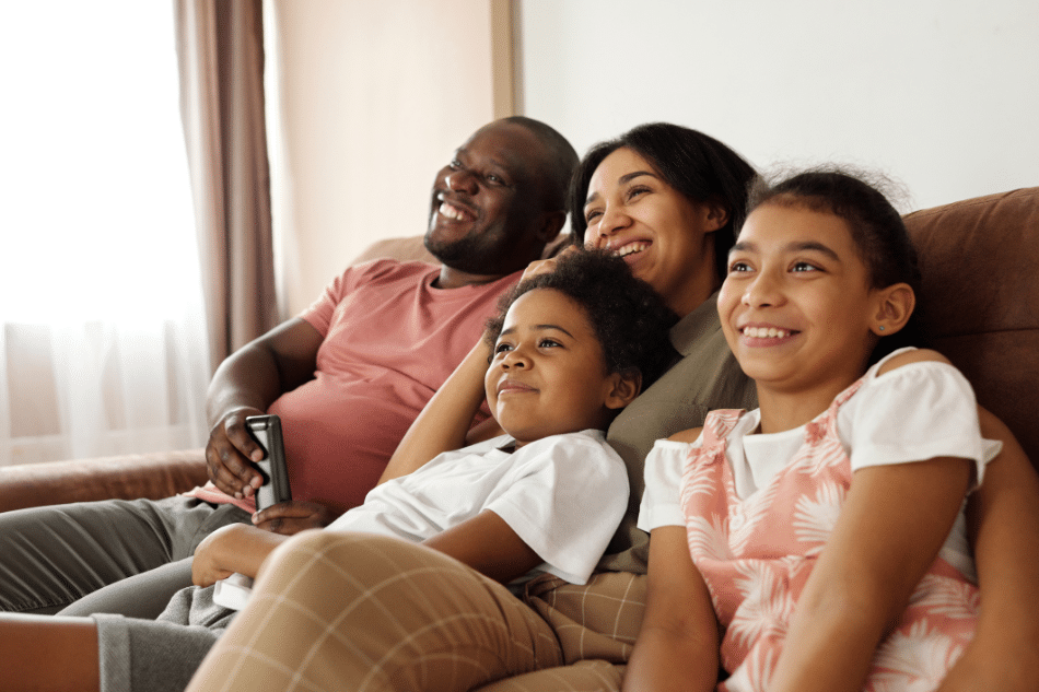 Father, mother, and two children smiling on the sofa after treatment for psychosomatic disorders in teenagers
