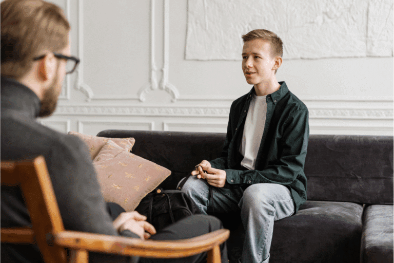 Teen boy sitting on couch across from male therapist during therapy session