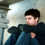 teenage boy sitting down with his knees to his chest needing adjustment disorder treatment for teens