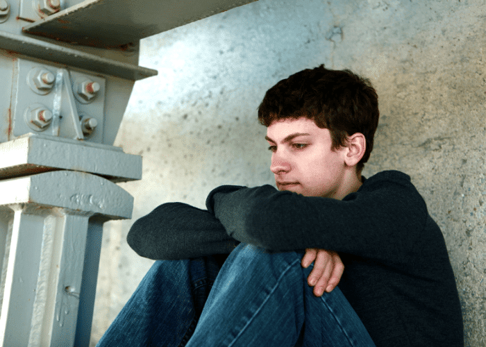 teenage boy sitting down with his knees to his chest needing Treatment for Adjustment Disorder in Teens
