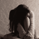 girl sitting on the floor looking down and holding her knees to her chest thinking about adjustment disorder in teens