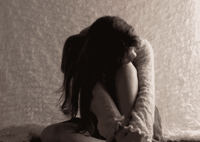 girl sitting on the floor looking down and holding her knees to her chest thinking about adjustment disorders in teenagers