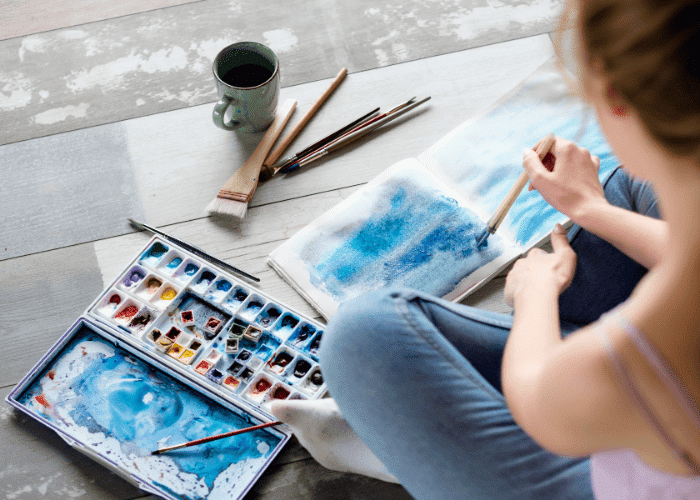girl painting a canvas with blue paint doing art therapy for emotional expression