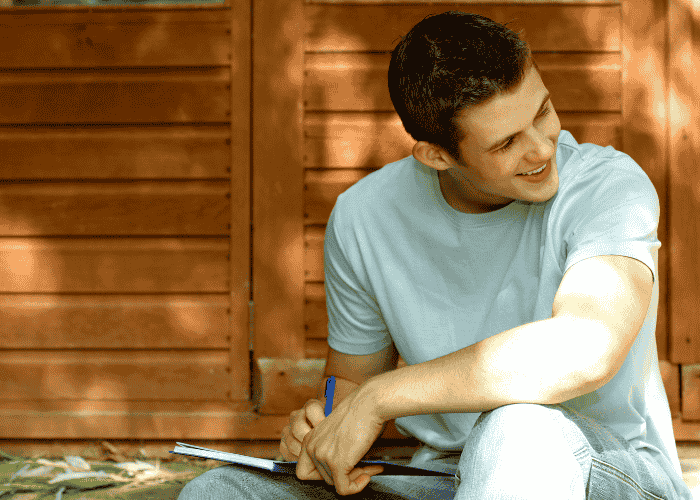 Teenage boy living with psychosomatic disorders sitting on a step outside journaling