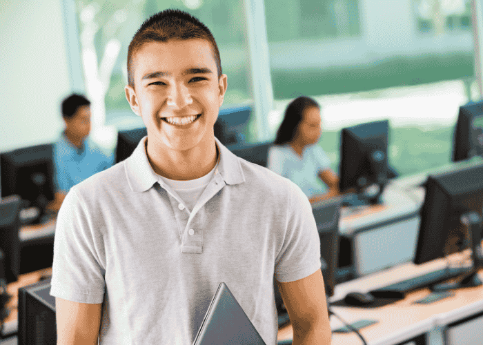 teenage boy smiling in school computer room after successful treatment for psychosomatic symptoms
