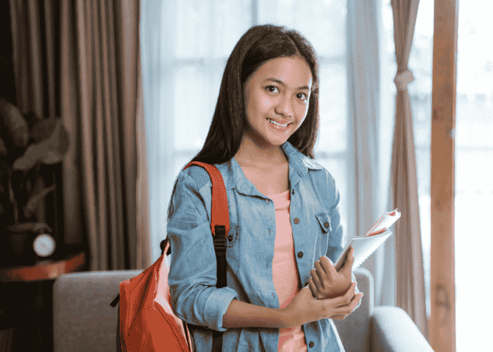 Teenage girl smiling with books in her hand after getting treatment for approval-seeking in teens