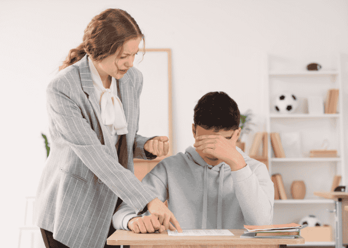 Teenage boy at school getting negative feedback on his work, struggling with approval-seeking in teens