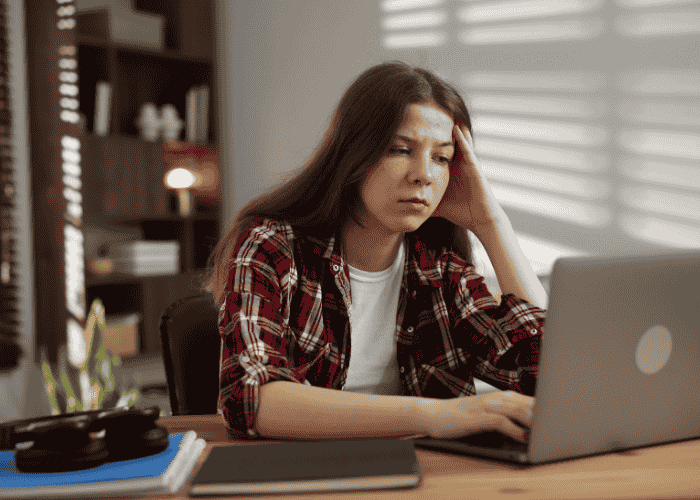teenage girl looking at her laptop with her hand on her head experiencing racing thoughts in teens