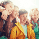 group of four teenagers standing outside looking off in the distance smiling