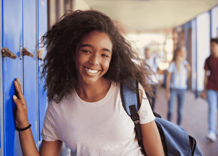 teenage girl smiling while leaning on her school locker after getting treatment for physical & stress-related symptoms in teens