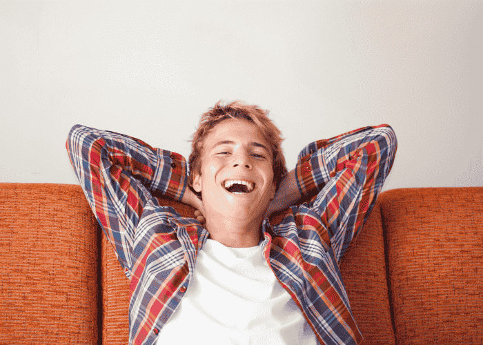 teenage boy leaning back on the sofa with his hands behind his head, looking relieved after getting support with cognitive issues in teens