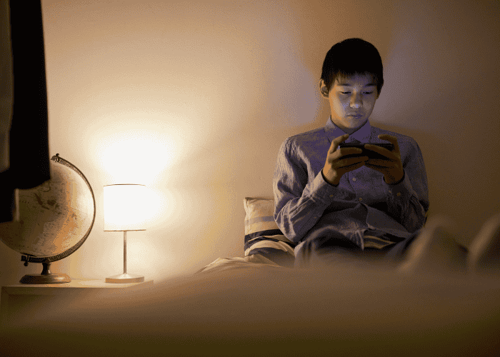 teenage boy looking at his phone while in his bedroom alone struggling with social & interpersonal symptoms in teens