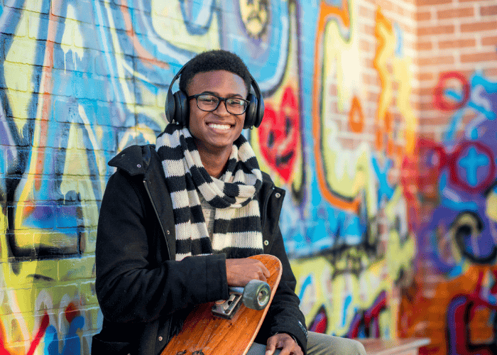 Teenage boy outside holding skateboard smiling after receiving treatment for crying spells