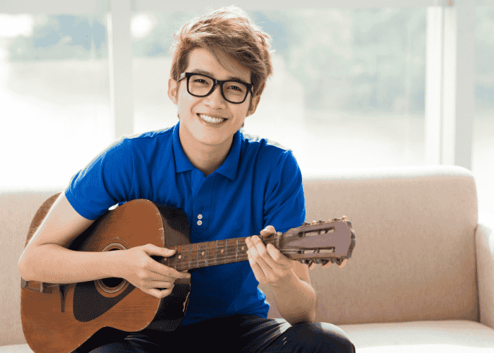 Teenage boy sitting on sofa smiling playing guitar after treatment for chronic fatigue