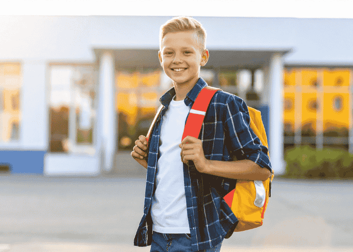 Teenage boy standing outside school holding backpack smiling after treatment for headaches in teens.