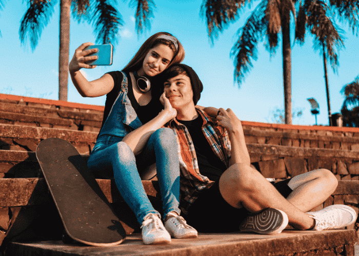 teenage boy outside at skate park sitting with teen girl posing for a selfie smiling after receiving support for teen trust issues