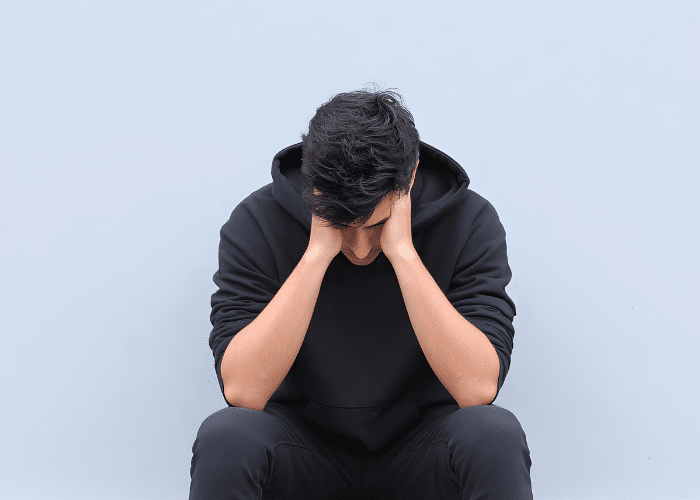 teenage boy sat by a wall with head in hands experiencing symptoms of teen codependency