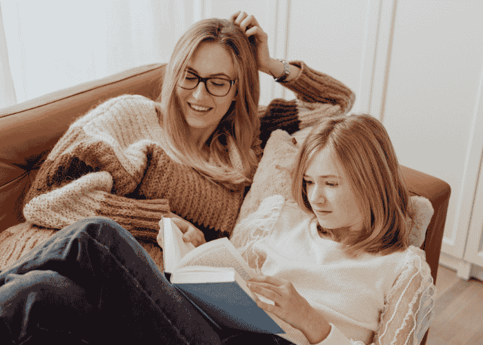 Teenage girl reading on sofa with mother after receiving treatment for teen social withdrawal