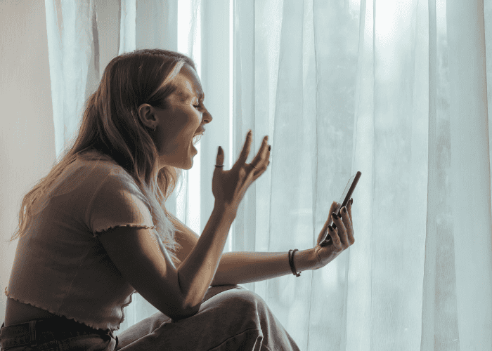 teenage girl sitting by a window with curtain drawn on a video call experiencing emotional overreactions in teens