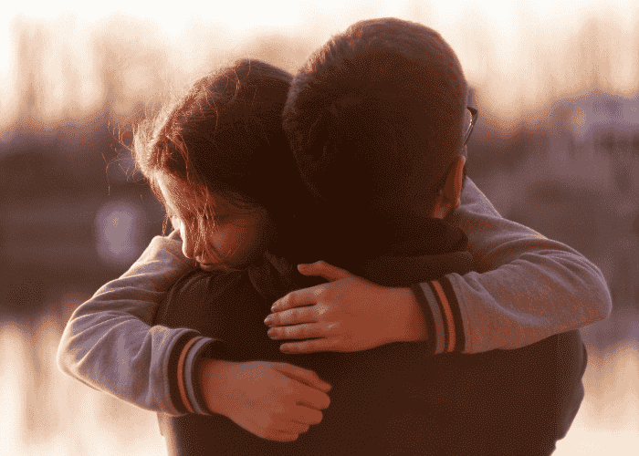 teenage girl hugging parent outside by a lake after receiving treatment for emotional overreactions in teens