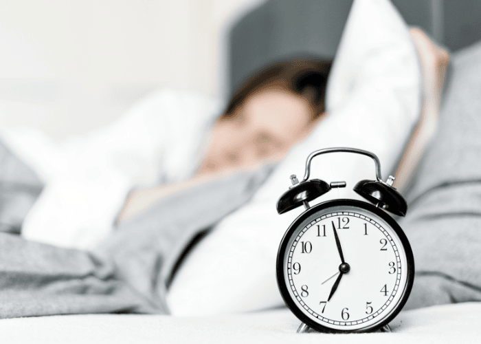 close up of alarm clock with teenage girl in bed experiencing sleep paralysis in teens in background