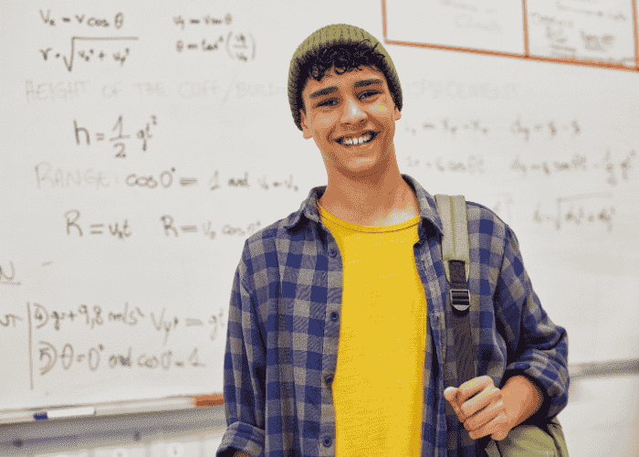 Teenage boy standing in classroom in front of whiteboard smiling after treatment for self-destructive behavior