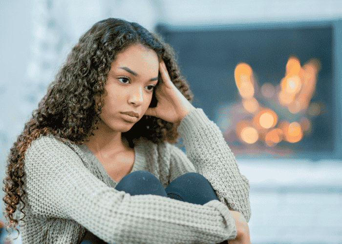 Teenage girl sitting by fire holding head in hand experiencing emotional numbness in teens.