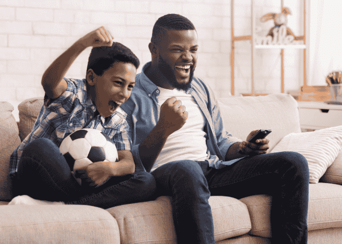 Teenage boy cheering watching soccer on TV with father after treatment for emotional numbness