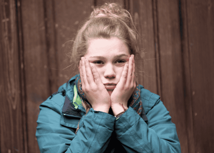 Teenage girl sitting with head in hands experiencing mood swings.