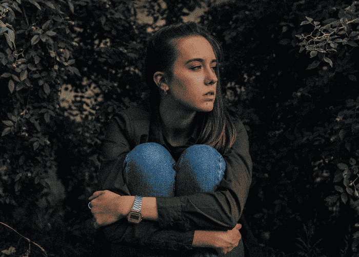 Teenage girl sitting outside with holding her knees into her chest because she's dealing with memory problems & brain fog in teens