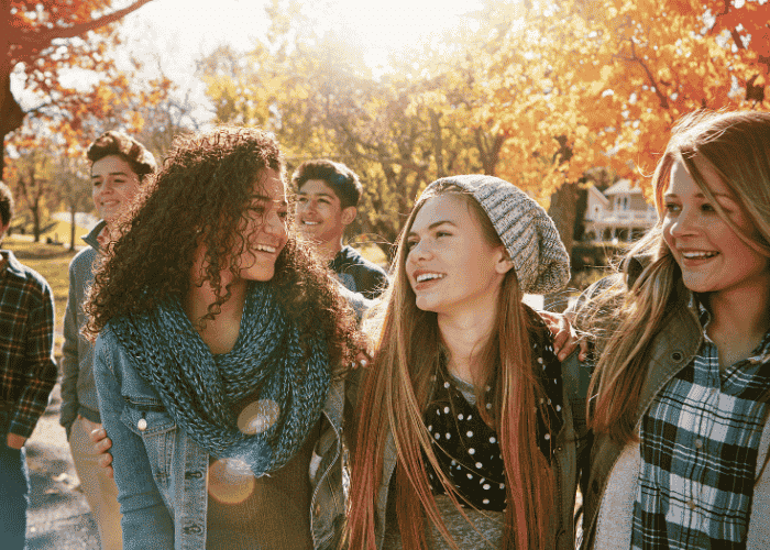 Group of three teenage girls in fall clothes walking outside smiling at each other after overcoming intrusive thoughts in teens