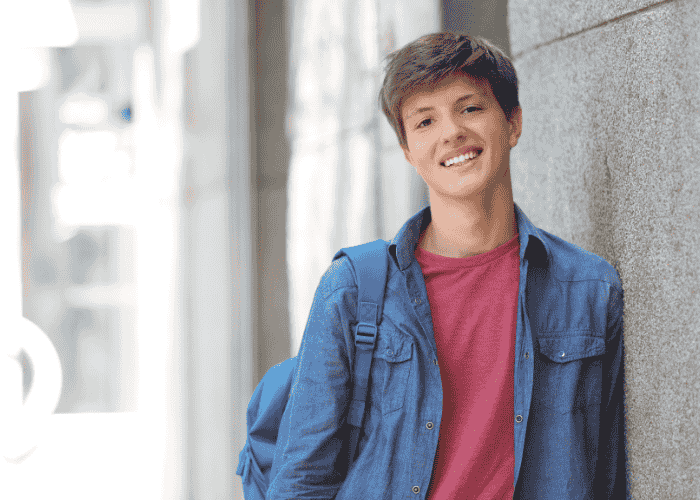 Teenage boy smiling while leaning against a wall after getting treatment for teen panic attacks