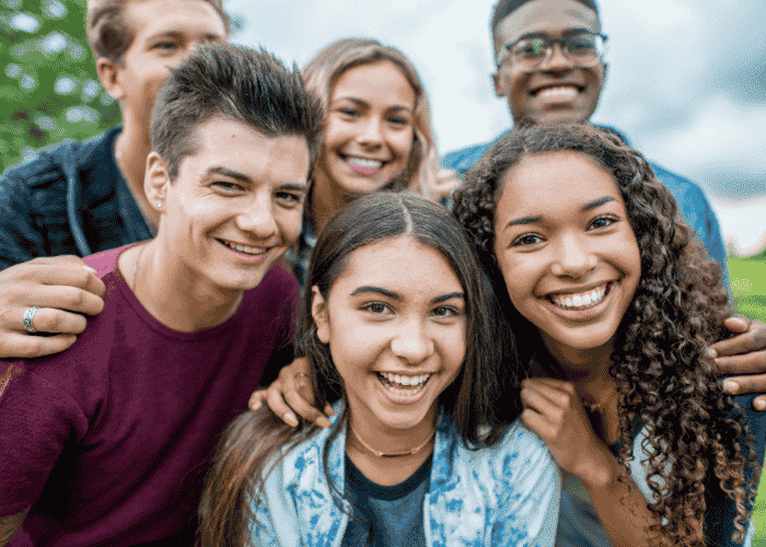 teenage girl outside at the park smiling with group of peers after support for feeling hopeless about the future