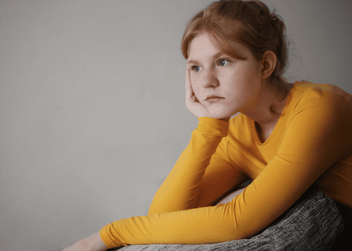 Teenage girl sitting with hear resting on her hand experiencing difficulty talking about feelings