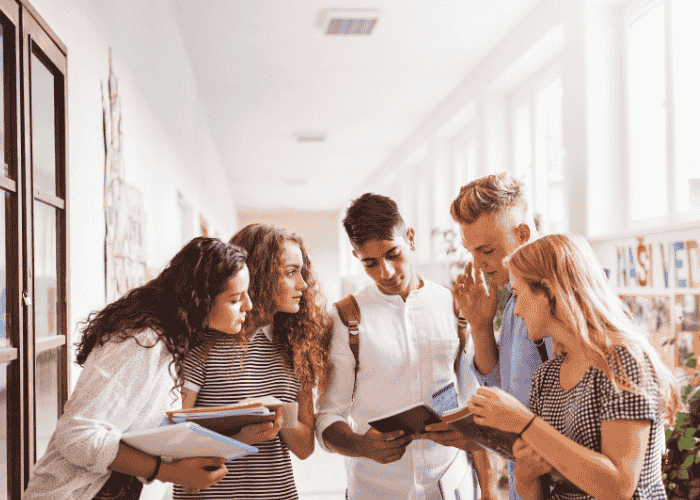 Teenage boy in school hallway comparing notes with a group of friends after support with all-or-nothing thinking in teens