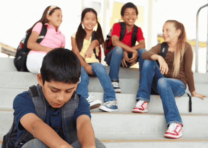 Teenage boy sat on steps in school looking down at the floor due to fear of being judged