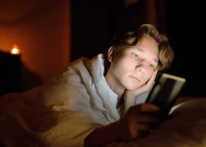 Teenage boy awake late in bedroom on phone due to losing track of time due to stress or anxiety