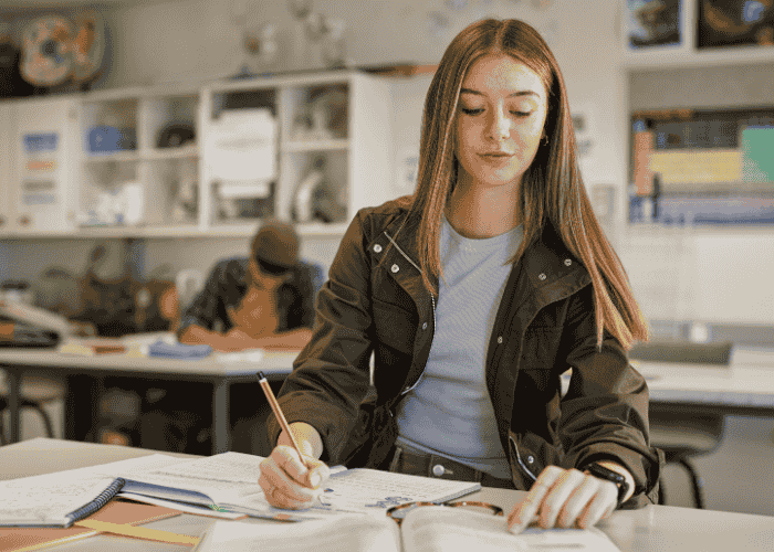 teenage girl sitting at desk looking at textbook in class smiling after treatment for restlessness in teens